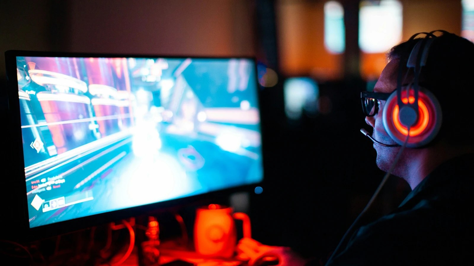 A gamer with a headset playing a fast-paced game on a PC monitor in a dark room
