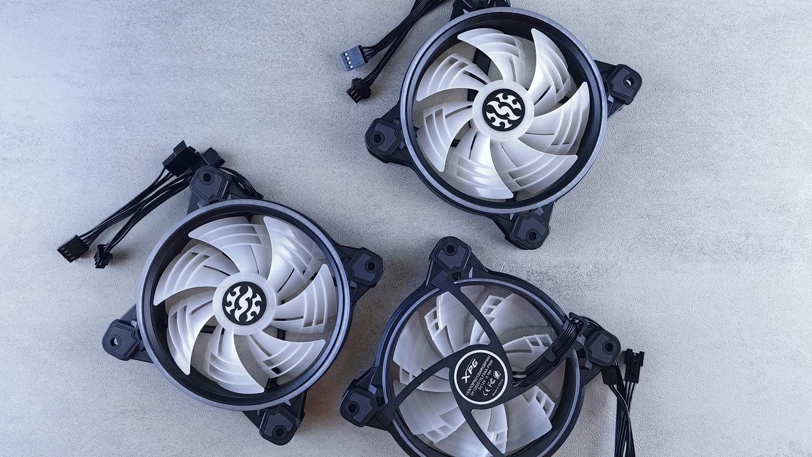 Three PC case fans with their cables on a gray surface
