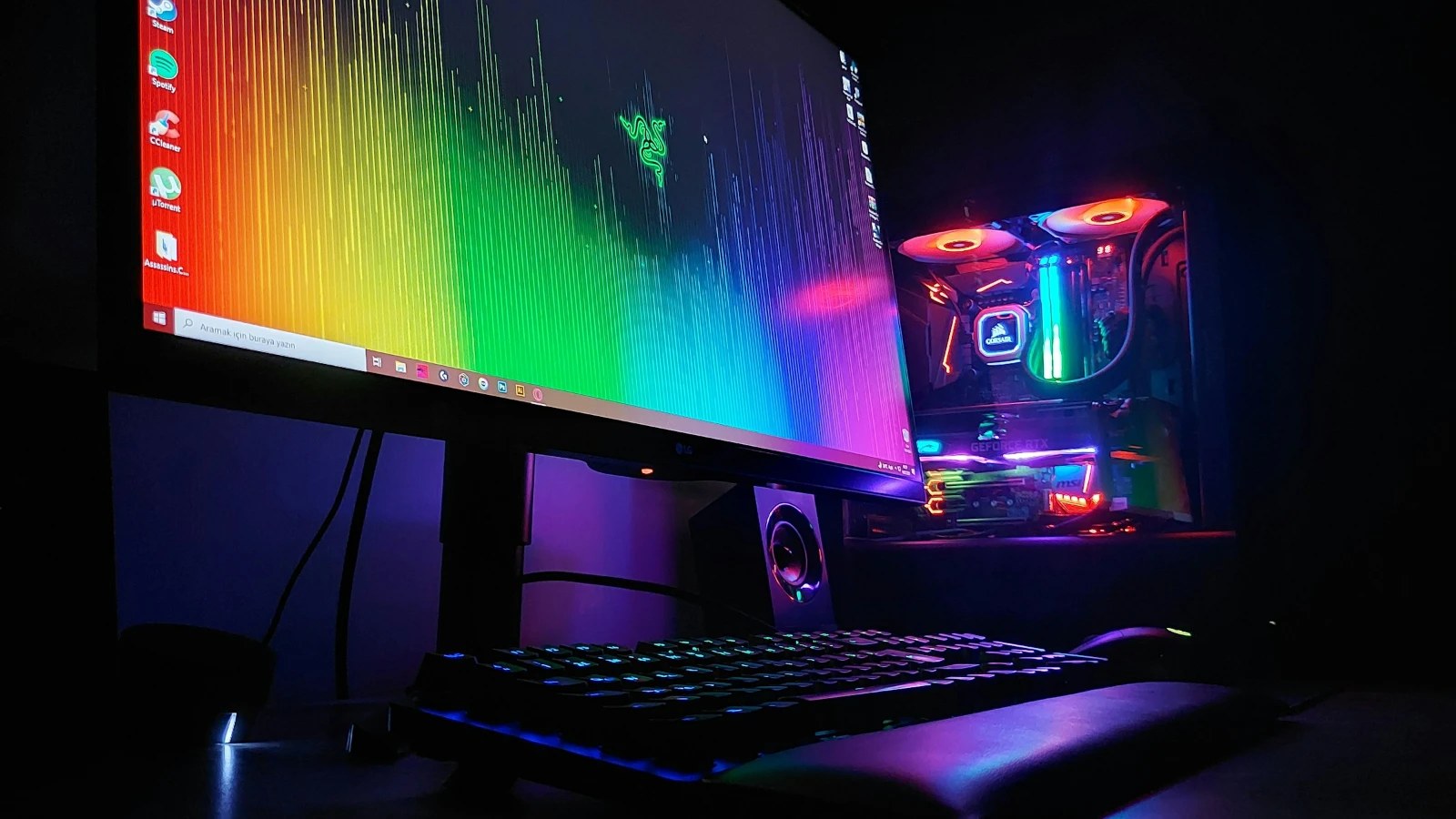A gaming monitor showing a colorful desktop next to a PC with RGB lighting