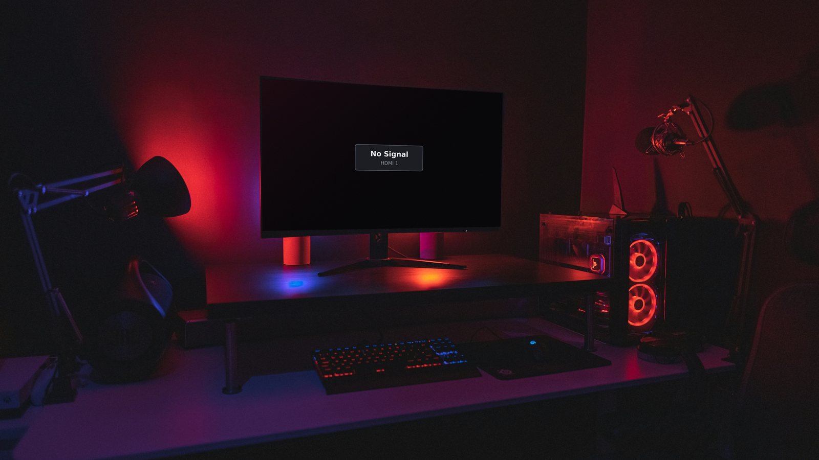 Gaming PC in a dark room with its fans lit up while the monitor shows a No Signal message